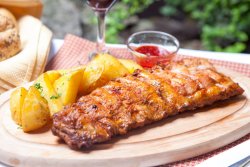Coaste de porc marinate pregătite la cuptor, servite cu cartofi aurii și sos bbq image
